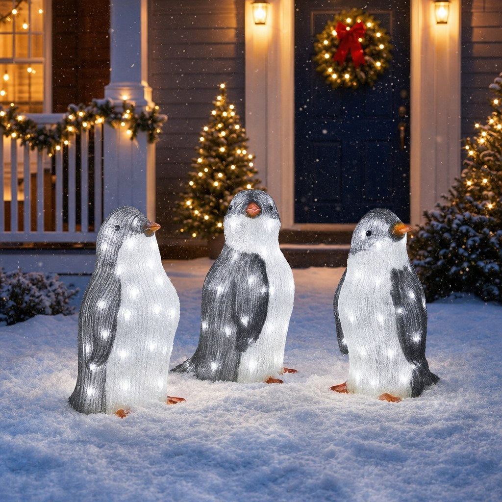 Glowing light-up acrylic penguin family in the snow in front of a house decorated for Christmas